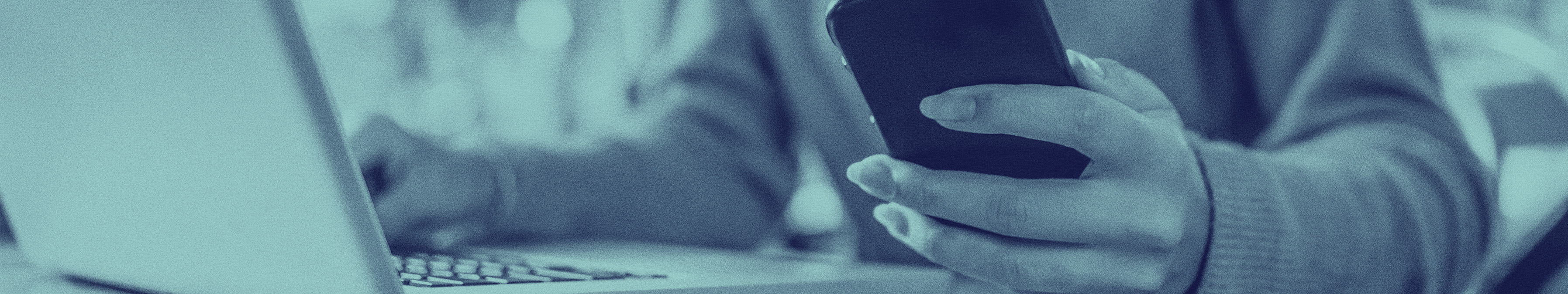 person holding phone up while working on computer