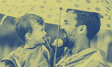 Father and son laughing, holding umbrella in the rain.