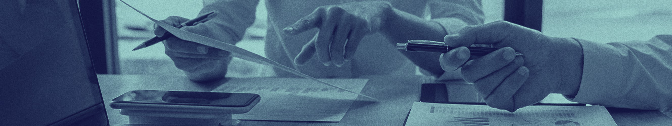 Hands holding papers and another hand with a pen pointing at a screen.