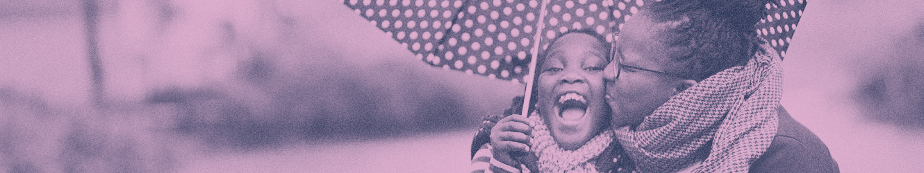 African American mother and daughter laughing and hugging under a polka-dot umbrella