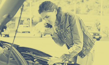 Woman looking under hood of broken down car